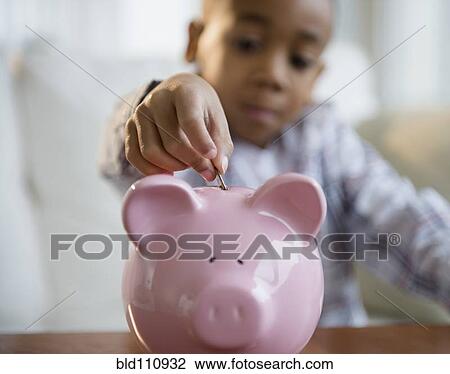Stock Image - African American boy putting coins in piggy bank. Fotosearch