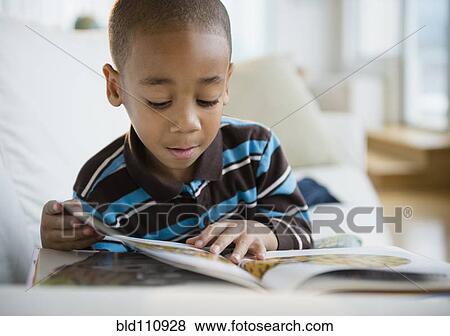 Stock Photo - African American boy reading book on sofa. Fotosearch