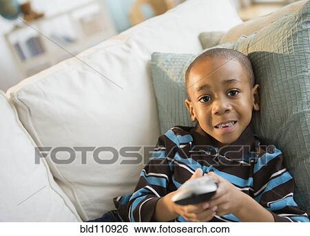 Stock Photograph - African American boy watching television on sofa. Fotosearch