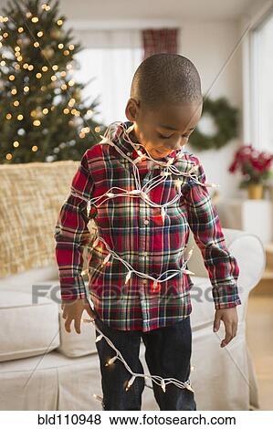 Stock Photo - African American boy wrapped in Christmas lights. Fotosearch