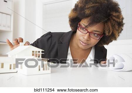 Picture - African American businesswoman working on model of house. Fotosearch