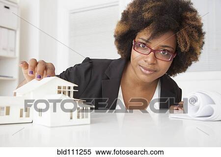 Stock Photography - African American businesswoman working on model of house. Fotosearch