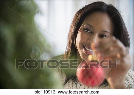 Stock Image - African American woman decorating Christmas tree. Fotosearch