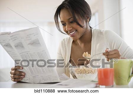 Stock Photo - African American woman reading newspaper at breakfast. Fotosearch