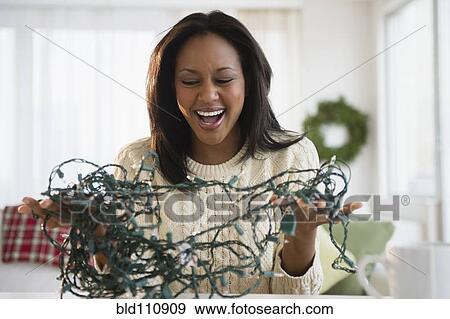 Stock Photo - African American woman untangling Christmas lights. Fotosearch