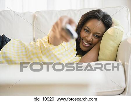 Stock Image - African American woman watching television on sofa. Fotosearch