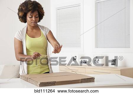 Picture - African American woman wrapping flat cardboard boxes. Fotosearch