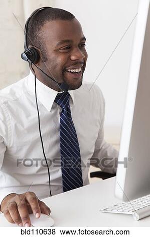 Stock Photo - Black businessman in headset working at desk. Fotosearch