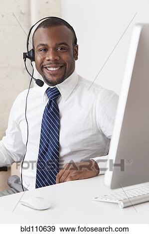 Stock Photo - Black businessman in headset working at desk. Fotosearch