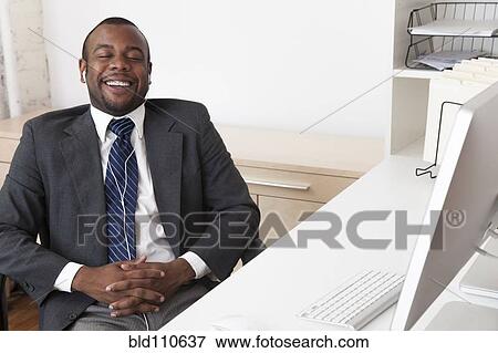 Stock Photo - Black businessman listening to music at desk in office. Fotosearch
