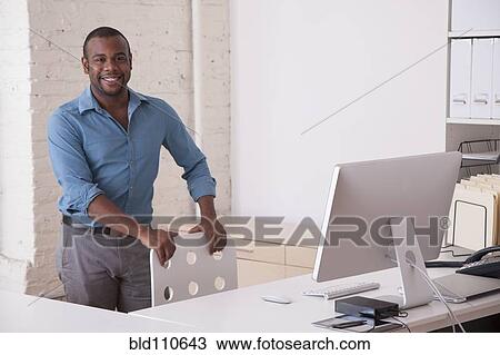 Stock Image - Black businessman standing at desk in office. Fotosearch