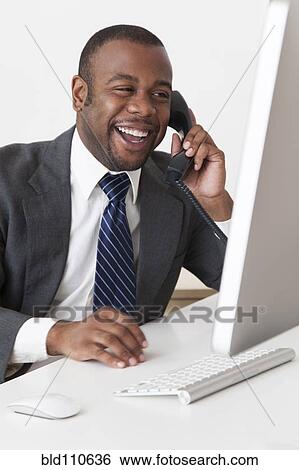 Stock Photograph - Black businessman talking on telephone at desk. Fotosearch