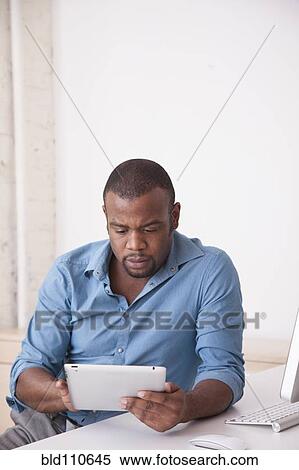 Stock Photography - Black businessman using digital tablet at desk. Fotosearch