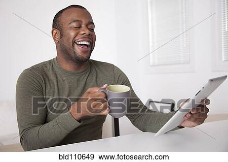 Stock Photo - Black man drinking coffee and using digital tablet. Fotosearch