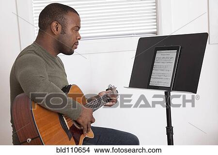 Picture - Black man practicing guitar with digital tablet. Fotosearch