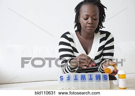 Stock Image - Black woman putting pills in organizer. Fotosearch