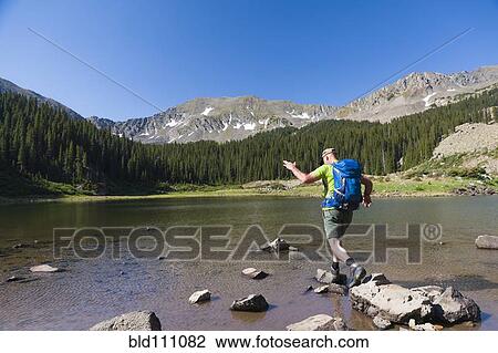 Stock Image - Caucasian hiker climbing on rocks in lake. Fotosearch