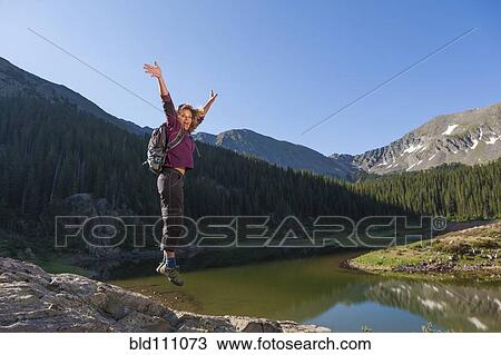 Stock Image - Caucasian hiker jumping for joy on boulder. Fotosearch