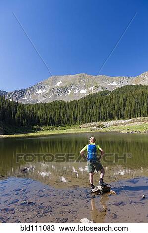 Stock Image - Caucasian hiker standing on rocks in lake. Fotosearch
