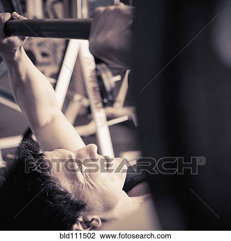 Stock Image - Caucasian man lifting weights in gym. Fotosearch