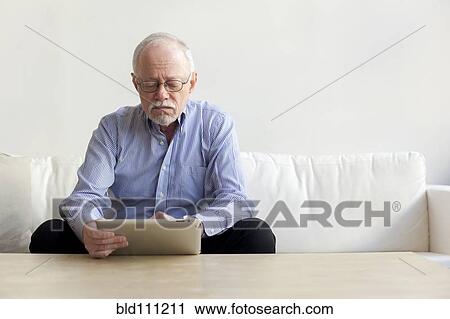 Stock Image - Caucasian man using tablet computer on sofa. Fotosearch