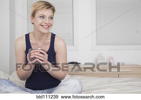 Stock Photo - Caucasian woman drinking cup of coffee on bed. Fotosearch