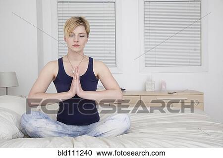 Stock Image - Caucasian woman meditating on bed. Fotosearch