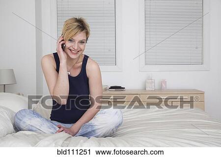 Stock Image - Caucasian woman talking on cell phone on bed. Fotosearch
