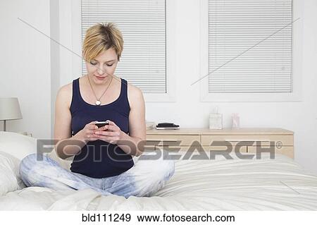 Stock Photo - Caucasian woman using cell phone on bed. Fotosearch
