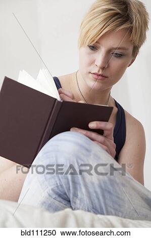 Stock Image - Caucasian woman writing in diary on bed. Fotosearch