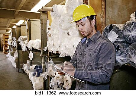 Stock Image - Caucasian worker checking product in warehouse. Fotosearch