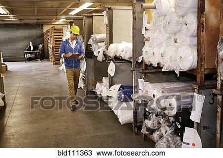 Stock Image - Caucasian worker checking product in warehouse. Fotosearch