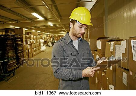 Stock Photo - Caucasian worker checking product in warehouse. Fotosearch