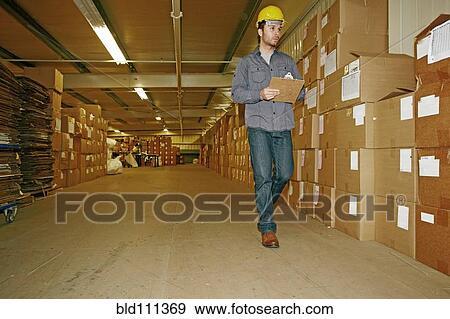 Stock Photo - Caucasian worker checking product in warehouse. Fotosearch