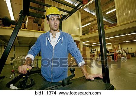 Picture - Caucasian worker driving machinery in warehouse. Fotosearch