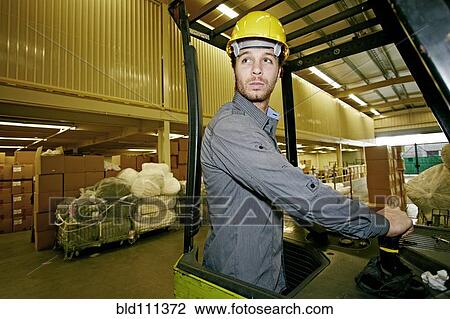 Stock Image - Caucasian worker driving machinery in warehouse. Fotosearch