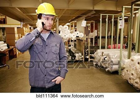 Caucasian worker talking on cell phone in warehouse View Large Photo Image Picture - Caucasian worker talking on cell phone in warehouse. Fotosearch