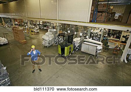 Stock Image - Caucasian worker talking on cell phone in warehouse. Fotosearch