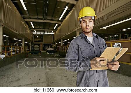 Stock Image - Caucasian worker with clipboard in warehouse. Fotosearch