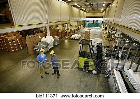 Stock Image - Caucasian workers talking in warehouse. Fotosearch