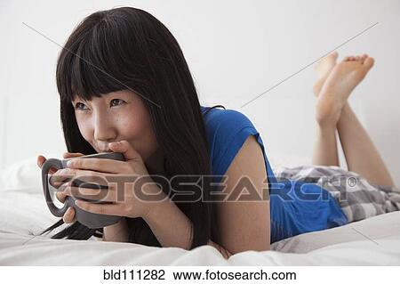 Chinese woman drinking cup of coffee on bed View Large Photo Image Stock Image - Chinese woman drinking cup of coffee on bed. Fotosearch