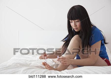 Stock Photo - Chinese woman painting toenails on bed. Fotosearch