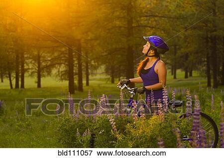 Stock Photo - Chinese woman pushing mountain bike in meadow. Fotosearch