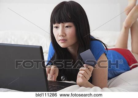 Stock Photograph - Chinese woman shopping online on bed. Fotosearch