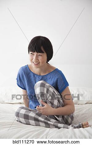 Stock Image - Chinese woman sitting on bed. Fotosearch