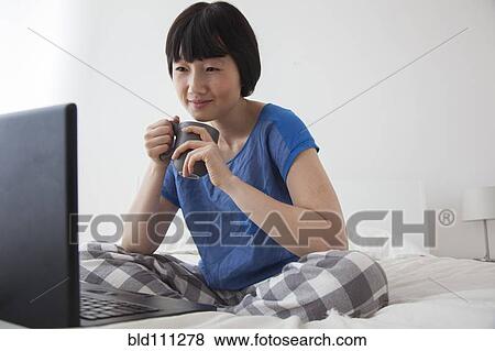 Stock Photo - Chinese woman using laptop on bed. Fotosearch