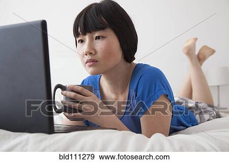 Stock Photo - Chinese woman using laptop on bed. Fotosearch