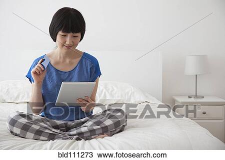 Stock Image - Chinese woman using tablet computer on bed. Fotosearch