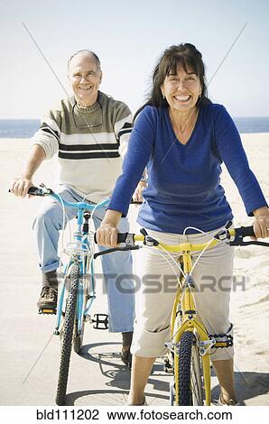 Stock Image - Couple riding bicycles on beach. Fotosearch