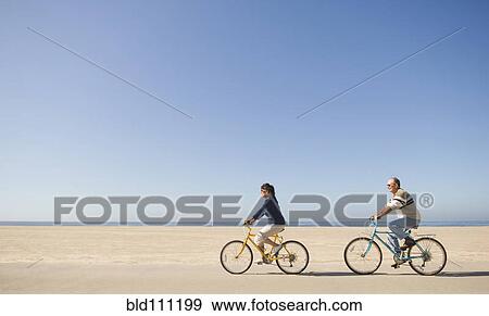 Stock Photo - Couple riding bicycles on beach. Fotosearch